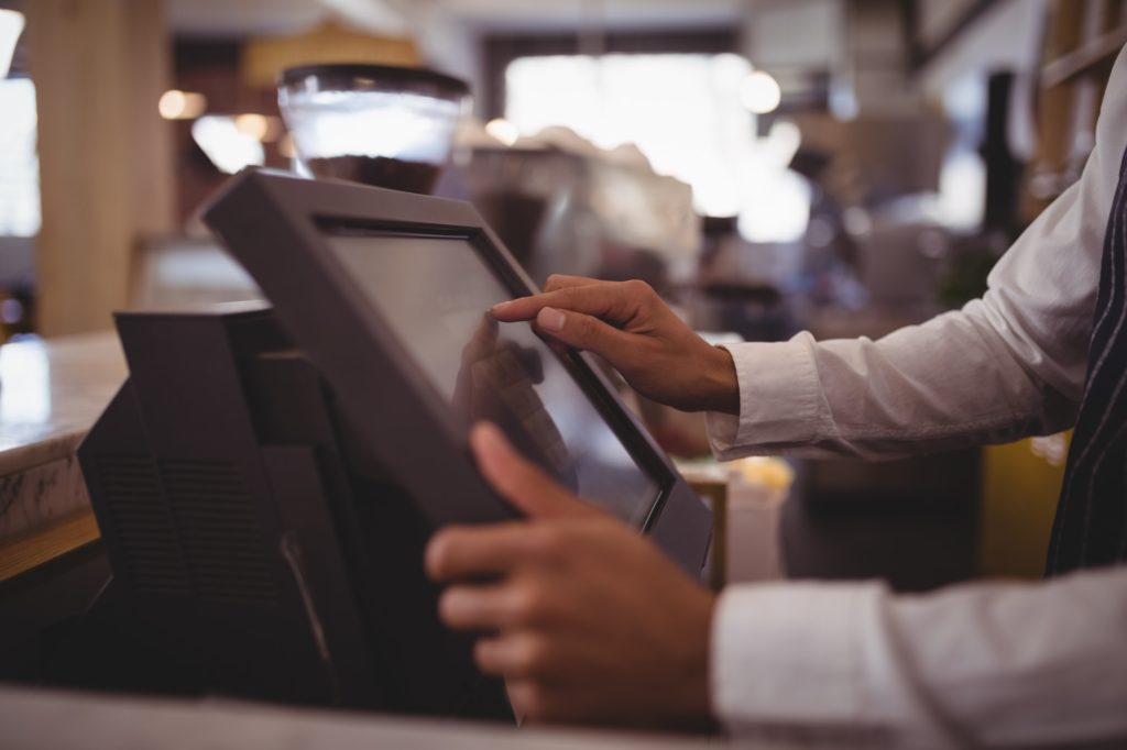 Midsection of waiter touching computer monitor at counter